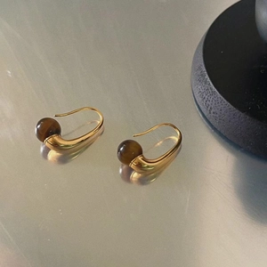 Detail view of gold tiger eye drop earrings on a sleek metallic surface