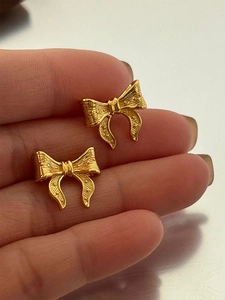 Detail of bow-shaped gold earrings with fine radial texture and vintage metallic finish