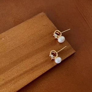 Detailed 45-degree angle view of gold pearl earrings with zircon on dark wood