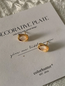 Détail de boucles d'oreilles dorées géométriques avec pierre sur une carte de support