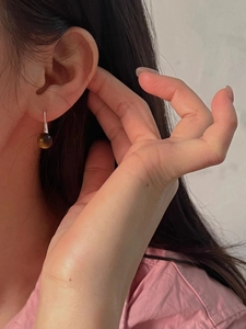 Detail of round tiger eye bead earrings with silver metal hooks worn by a model
