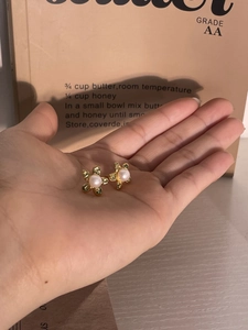 Detailed close-up of a golden flower earring with a white pearl center in hand