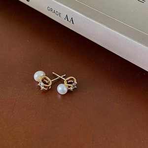 Close-up of gold pearl stud earrings with zircon stones on a leather surface