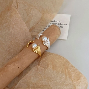 Detail of gold and silver textured shell rings with pearls on a wooden stand
