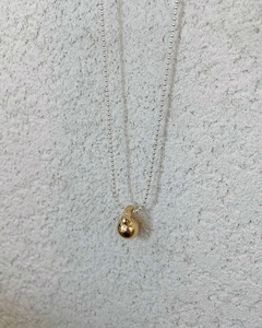 Close-up of minimalist gold sphere pendant on a silver bead chain with macro texture