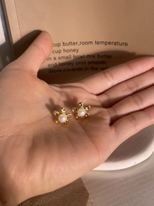 Detail of vintage gold flower stud earrings with white pearl center held in hand