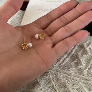 Close-up of gold pearl zircon stud earrings held by hand over a white knit background