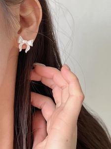 Silver bow stud earrings with textured metallic finish shown on model in minimalist style