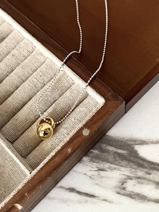 Detail of a polished gold ball pendant on a silver beaded chain in a wooden jewelry box