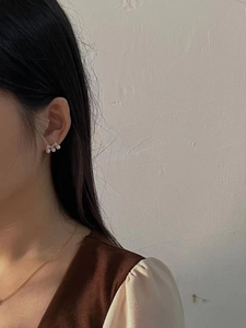 Close-up of minimalist gold earrings with three white round pearls worn by a model