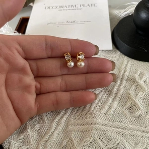 Close-up of elegant gold earrings featuring a white pearl and sparkling zircon crystal