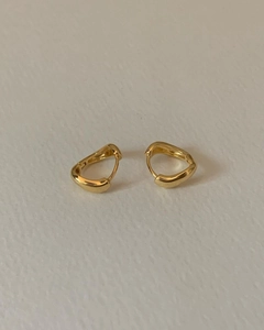 Macro detail of gold irregular wave hoop earrings with a mirror-polished liquid metal finish