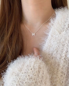 Close-up of 925 sterling silver bow pendant necklace worn on a white knit sweater