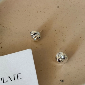 Macro detail of pumpkin shaped 925 sterling silver studs with radial ridges on ceramic tray