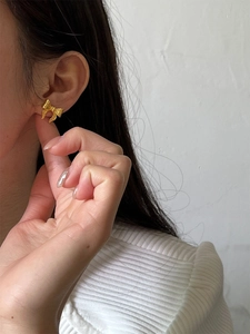 Close-up of a model wearing a minimalist gold bow earring with a matte metallic finish