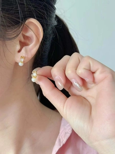 Close-up of elegant gold pearl earrings with cubic zirconia on a female model ear