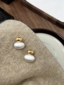 Close-up of gold and silver plated earrings with oval opal on soft cashmere fabric