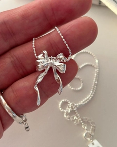Gros plan sur un collier avec pendentif noeud en argent 925 tenu dans la main