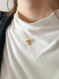 Detail of matte gold trophy pendant necklace on model wearing white turtleneck
