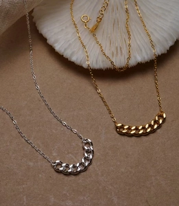 Dettaglio macro di collane a maglia cubana oro e argento su un supporto a conchiglia