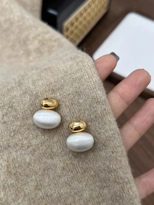 Macro shot of gold and white bean earrings on tweed fabric held by a hand
