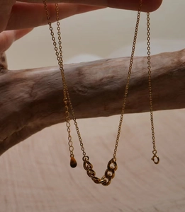 Dettaglio della collana d'oro con maglie intrecciate esposta su un ramo di legno