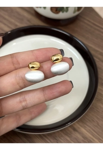 Detail of two-tone metal earrings with gold glossy ball and silver brushed oval texture