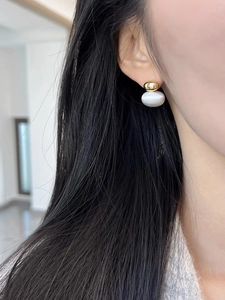 Minimalist gold ball and white cat eye bead drop earrings worn by a model in soft light