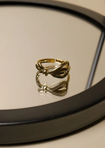 Close-up of golden adjustable bow ring with high-polish finish reflecting on a black mirror