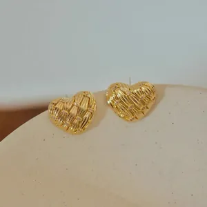 Close-up of golden heart earrings with radial textures and small crystal diamonds