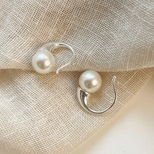 Macro shot of minimalist S925 silver hook earrings with white pearls on linen