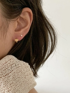 Detail of a golden bow earrings with brushed texture and mini pearl stud on an ear