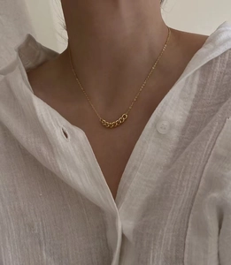 Dettaglio di una collana a catena cubana dorata indossata con una camicia di lino bianca