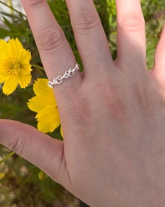 Détail de la bague coeur infini en argent sur le doigt avec fleurs jaunes en fond