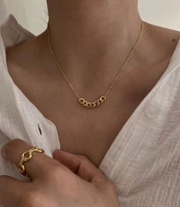 Dettaglio di una collana a catena dorata lucida e anello coordinato indossati dal modello