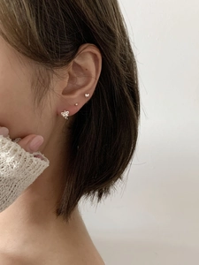 Close-up of three 925 sterling silver studs with heart and bow icons on a female ear