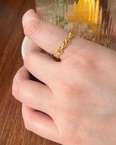 Détail d'une bague à maillons en forme de cœur dorée portée avec un décor chaleureux