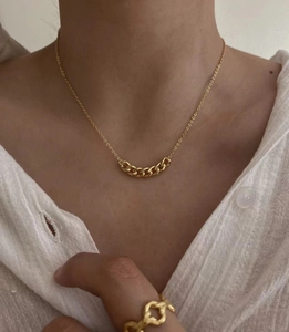 Dettaglio di collana a catena dorata e anello intrecciato con camicia di lino
