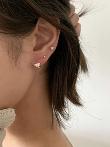 Close-up of 925 sterling silver bow, heart, and dot stud earring set on female ear