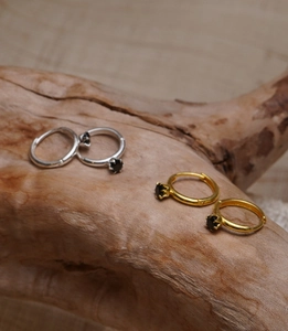 Detail of silver and gold 925 silver huggie earrings with black cubic zirconia on driftwood
