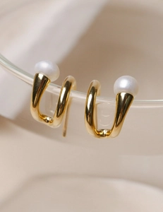 Detail of gold minimalist twist earrings with pearls on transparent glass edge