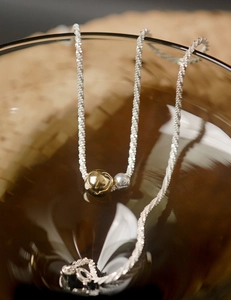 Macro detail of mixed-metal gold and silver bead pendant on a textured twist chain