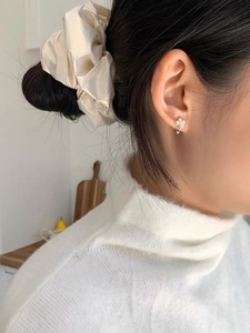 Gros plan de boucles d'oreilles fleur S925 et chouchou en satin portés par un mannequin