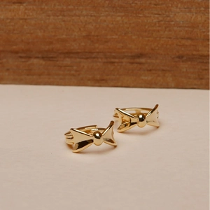 Elegant gold bow-shaped hoop earrings with polished finish on a minimalist wooden base