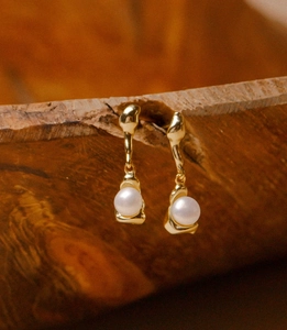 Macro shot of gold-plated irregular metal earrings with white pearls on a wood surface