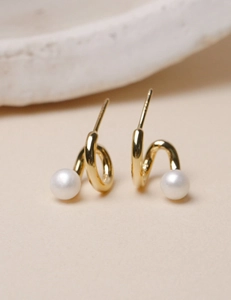 Macro shot of gold spiral stud earrings with white pearls on a minimalist background