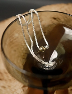 Detail of silver-toned chain with gold and silver beads draped on glass rim