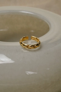 Detail eines minimalistischen Gold-Flechtrings mit polierter Oberfläche auf Keramik
