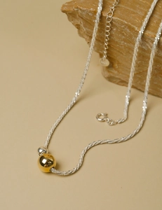 Detailed shot of mixed gold and silver beads on a twisted silver chain over a textured stone