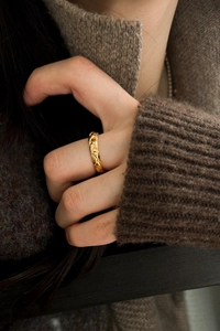 Detailaufnahme eines goldenen Rings mit Rautenmuster, am Finger getragen vor Strickhintergrund